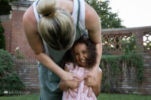 Mom tickling little girl who is laughing at rose garden park in Beverly