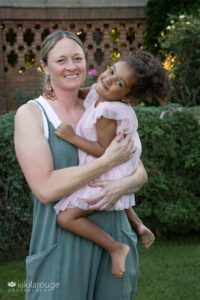 Blonde woman in green jumper laughing with daughter in pink dress