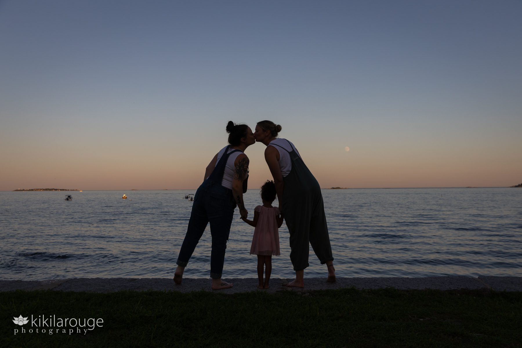 Couple kissing at sunset holding had of their daughter in silhouette