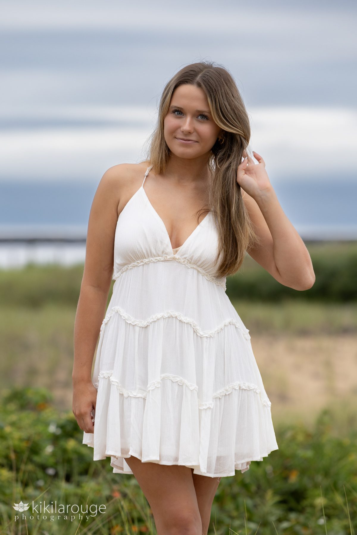 Teen senior girl in white dress dancing in beach dunes hand in hair