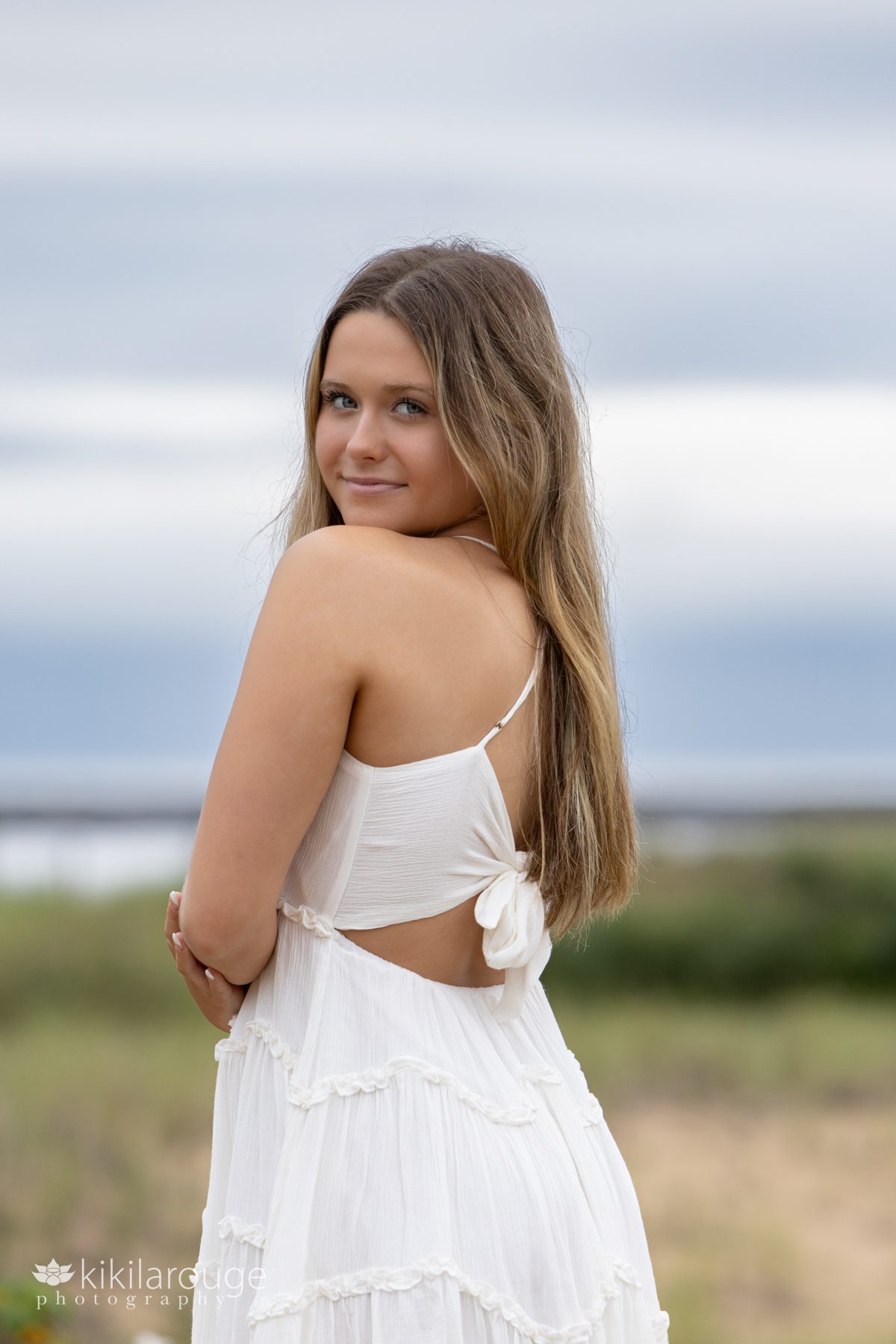 Girl with white dress with bows on back looking over shoulder for senior portrait Plum Island