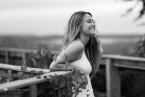 Teen girl in white dress leaning on beach boardwalk with one hand in hair laughing