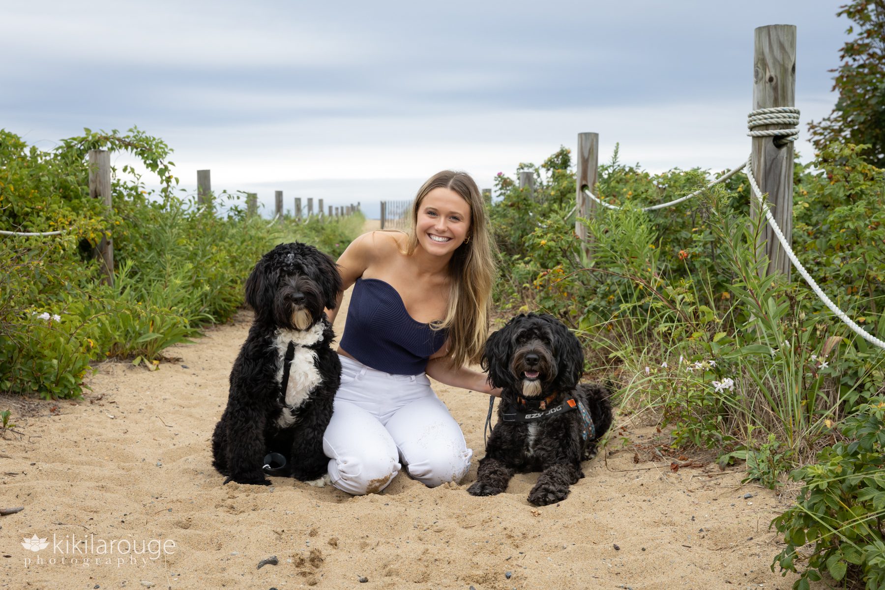 Senior girl in white jeans and blue tank top with two Portuguese water dogs
