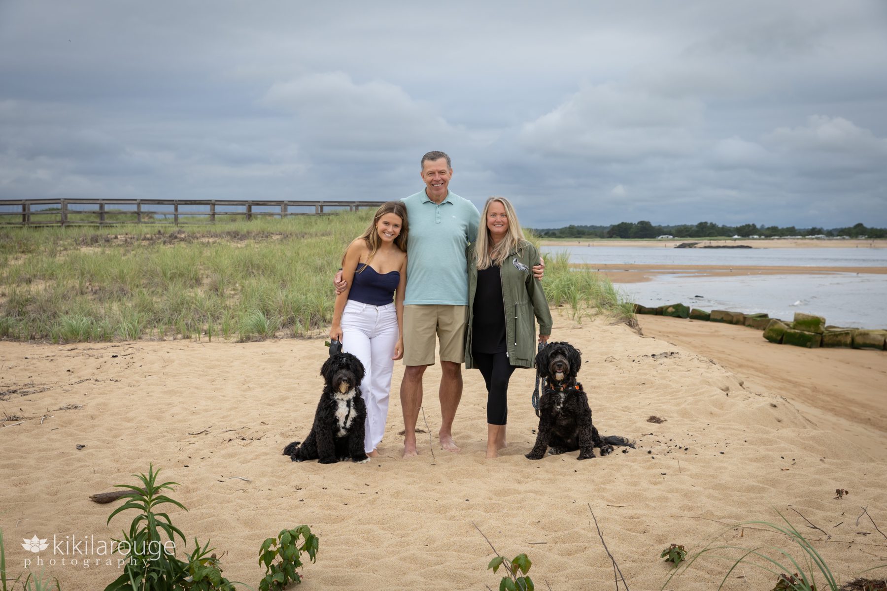 Senior girl in white jeans and blue tank top with Mom and Dad and two Portuguese water dogs on Plum Island Beach standing in dunes