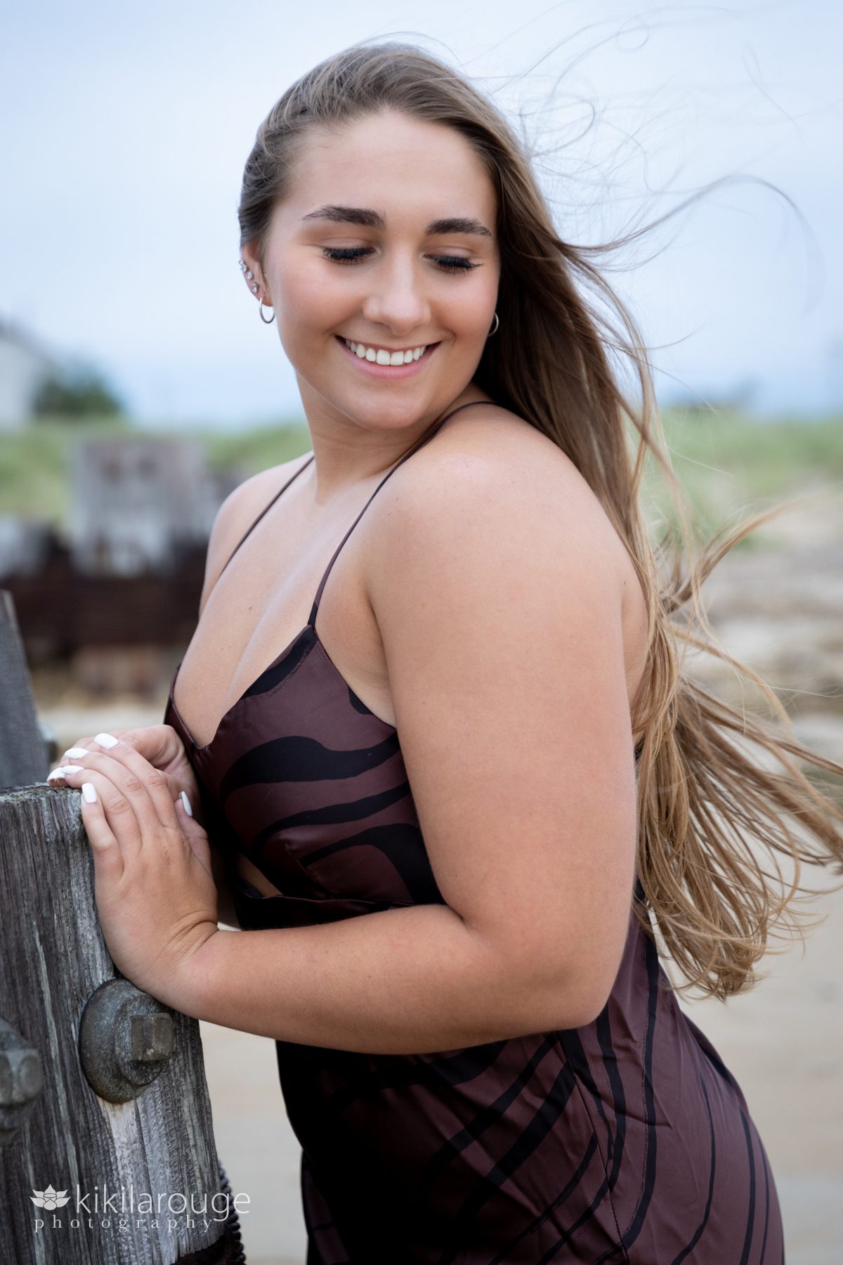Girl in brown dress with hair blowing at Plum Island Beach looking down