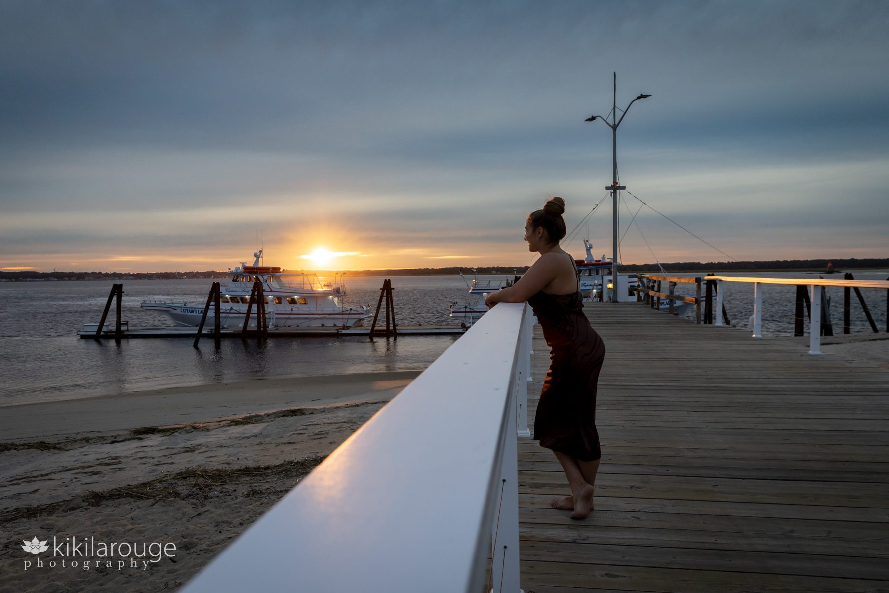 Silhouette of senior girl in brown dress on dock at sunset