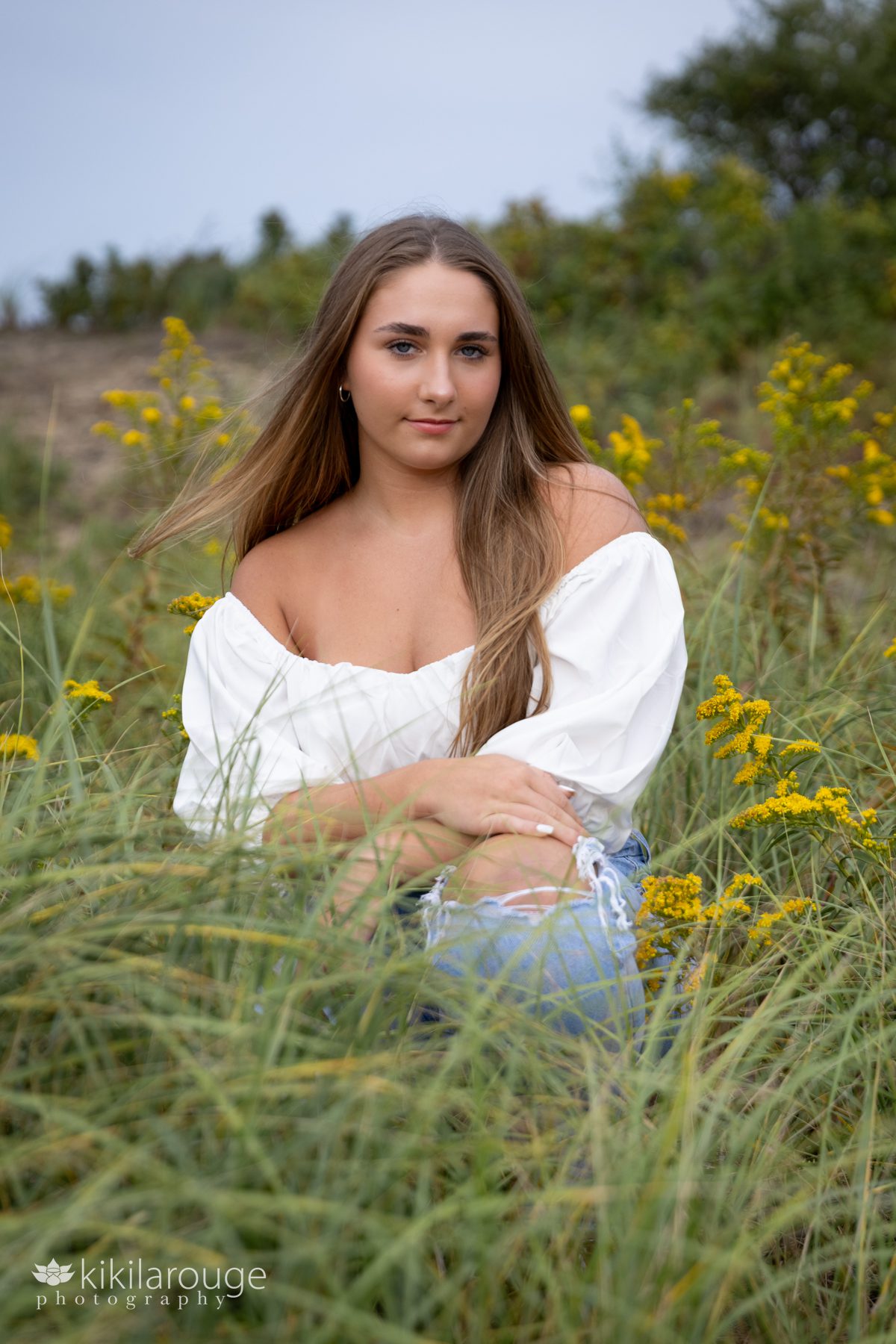 Triton Senior Portrait Girl in Jeans with white top tied in back at beach sitting in dunes with goldenrods
