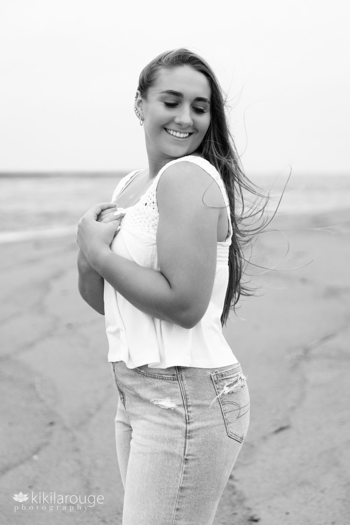 Triton Senior Portrait Girl in Jeans with white top tied in back at beach BW looking down in jeans