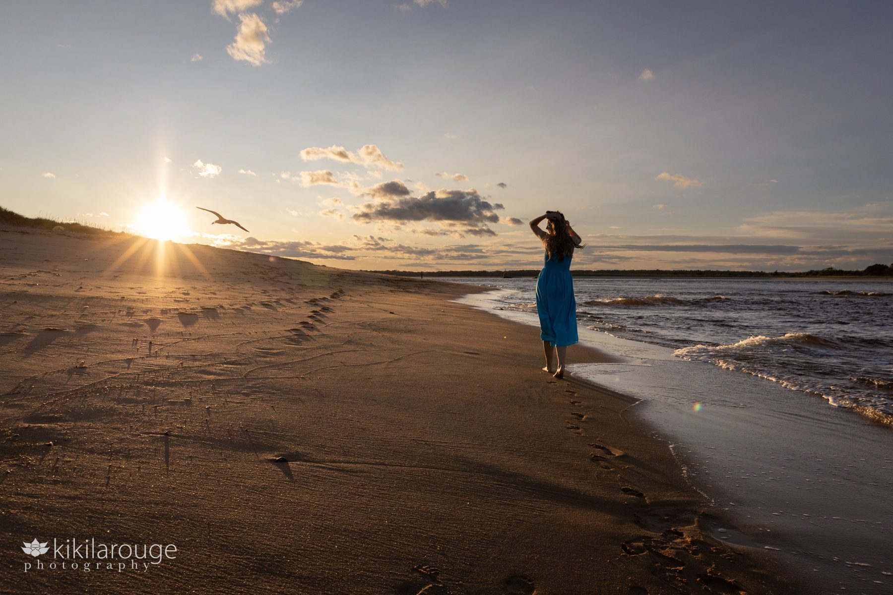 Teen girl in long aqua blue dress walking into the Plum Island sunset with bird flying by