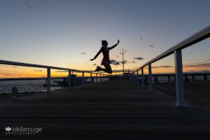 Teen girl in Irish Step Dancer outfit jumping in silhouette with feet behind on the plum Island pier