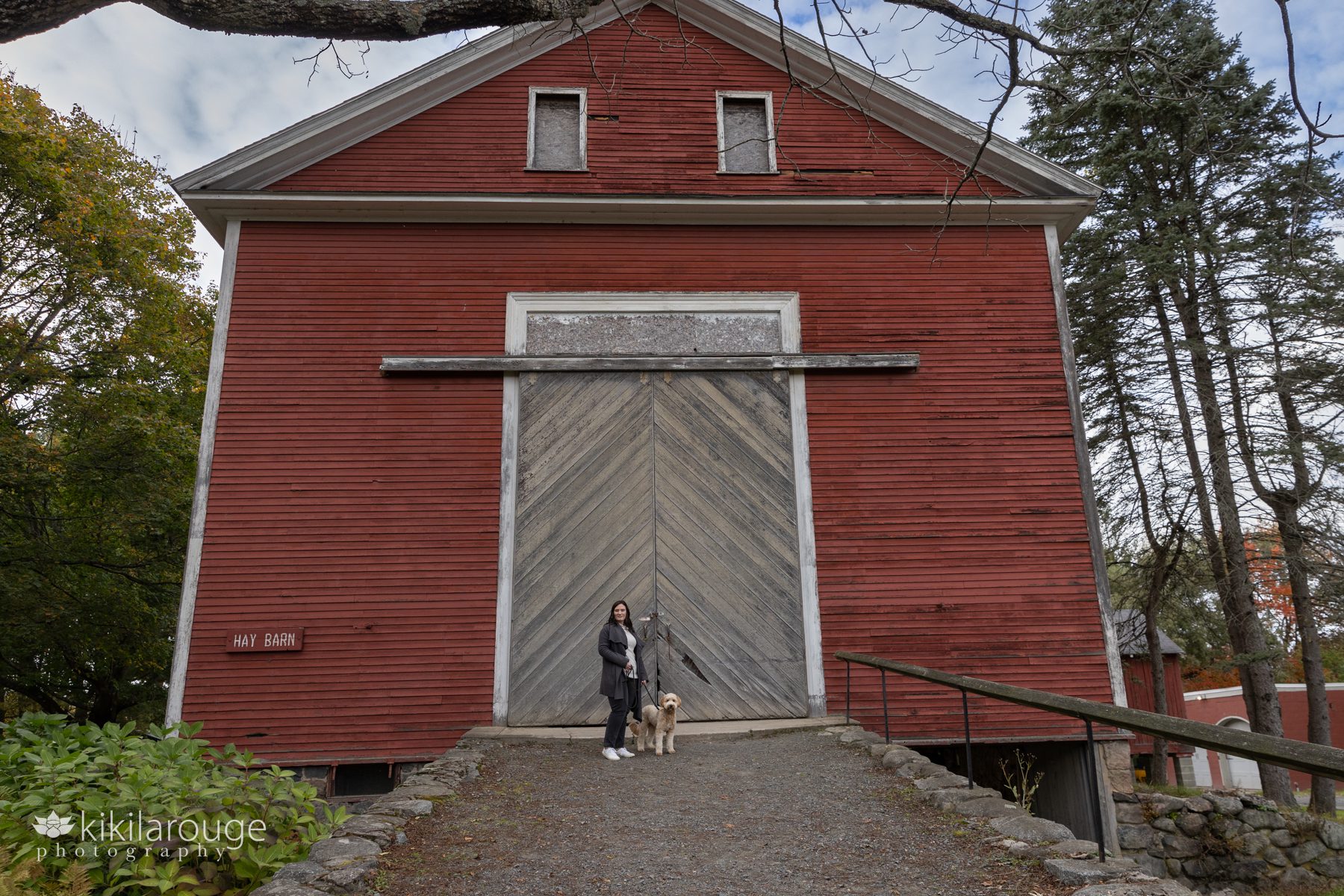 Woman with her labradoodle in front of a big red barn at Endicott Park Danvers
