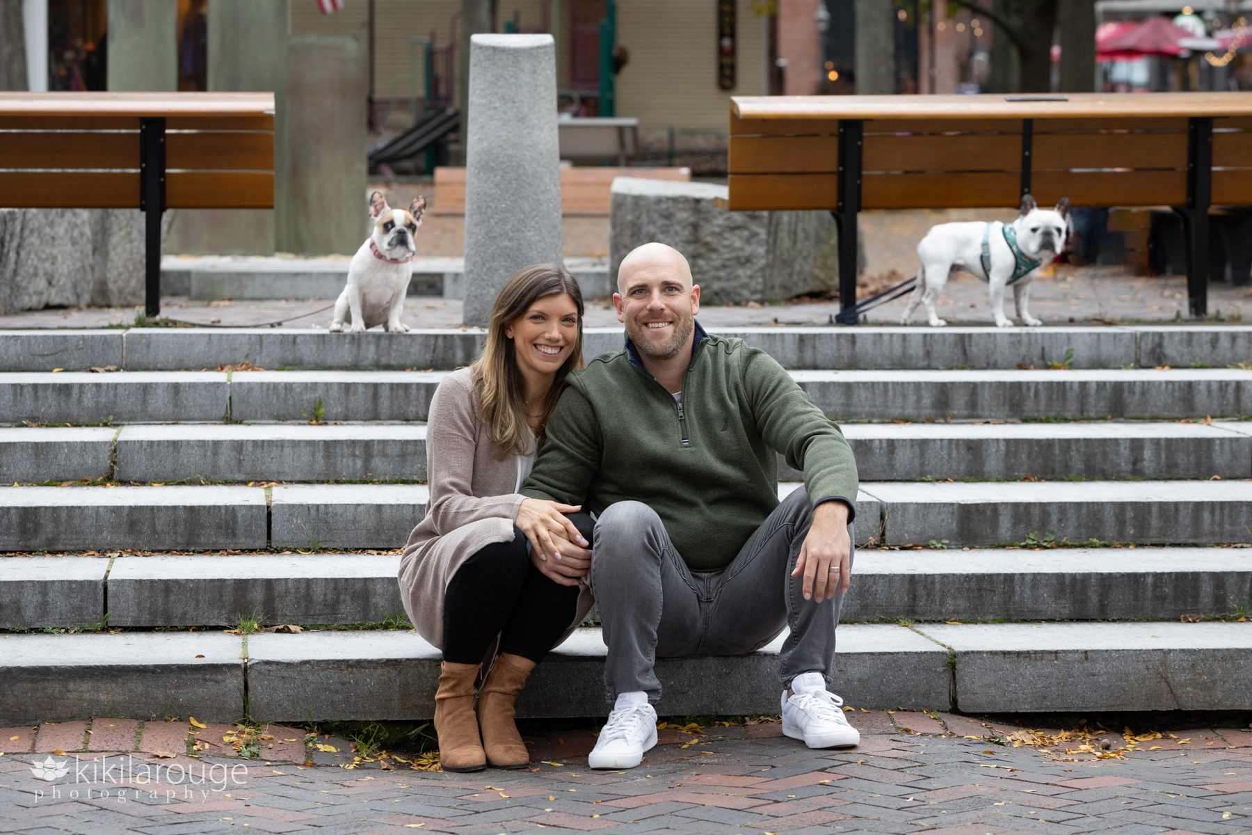 Couple sitting on cement steps with their two French Bulldogs in the background