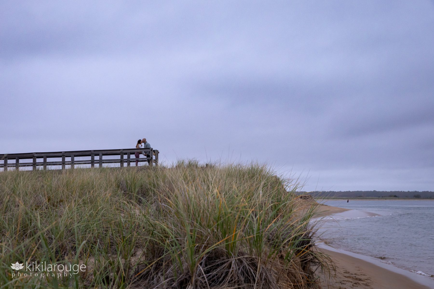 Landscape view of Plum Island beach with a couple in silhouette on the end of the boardwalk in the distance kissing