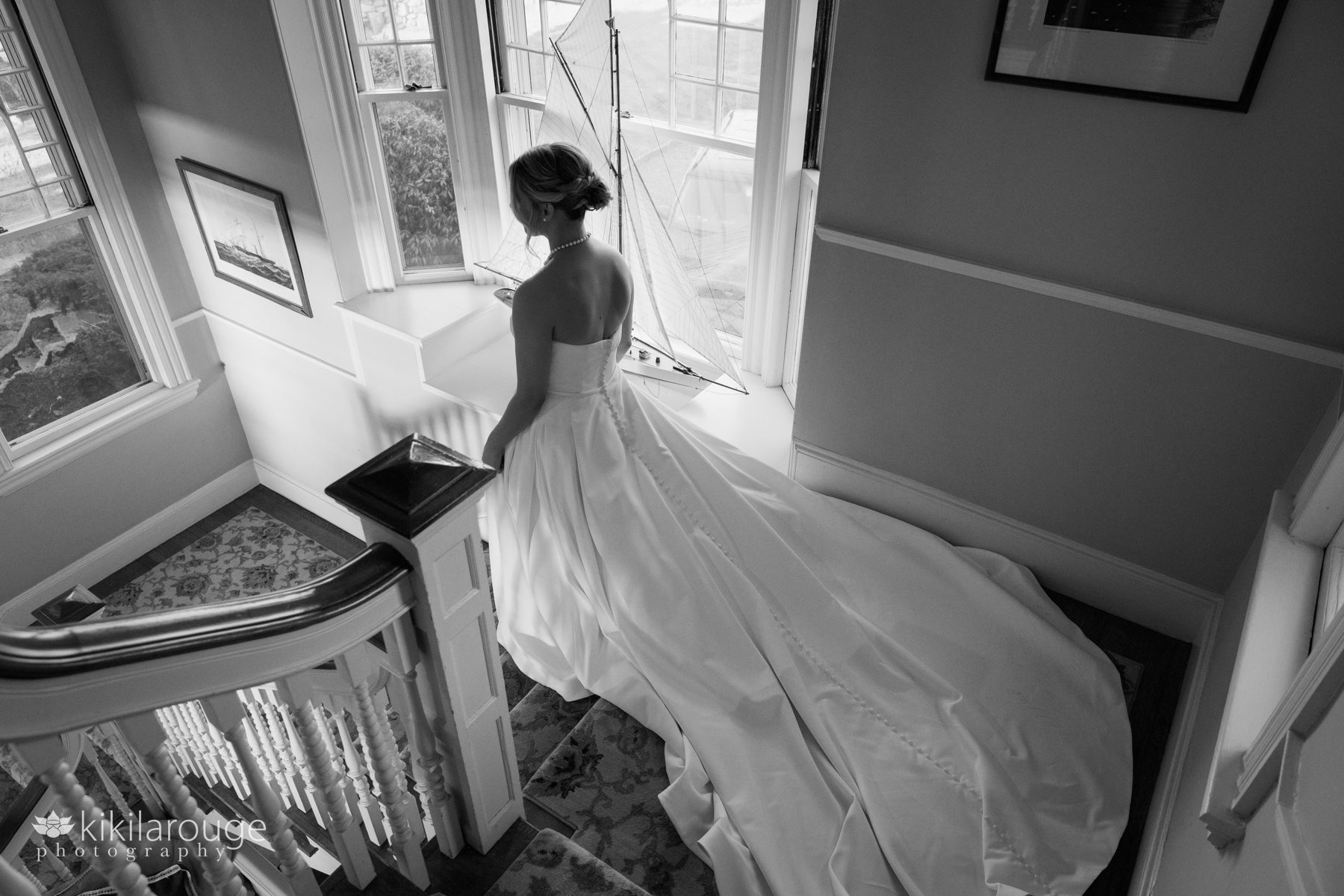 BW bride and wedding gown train going down yacht club stairs with boat replica in window panel