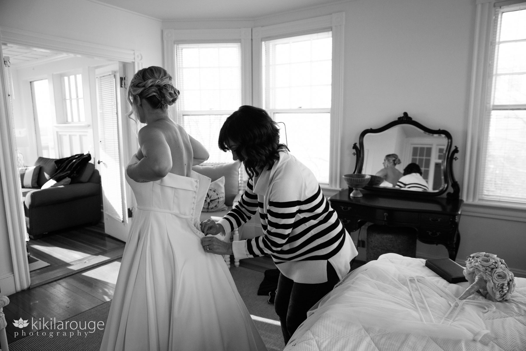 BW of Mom in striped sweater zipping up the back of her daughter's wedding gown