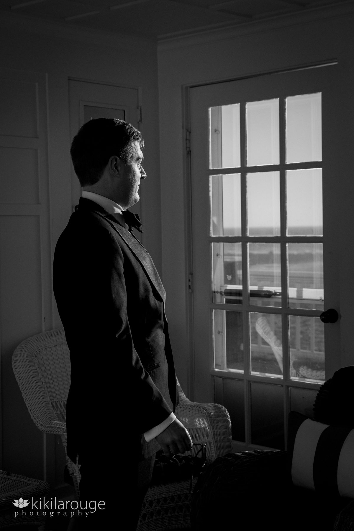 Groom in silhouette and profile looking out yacht club windows to the ocean