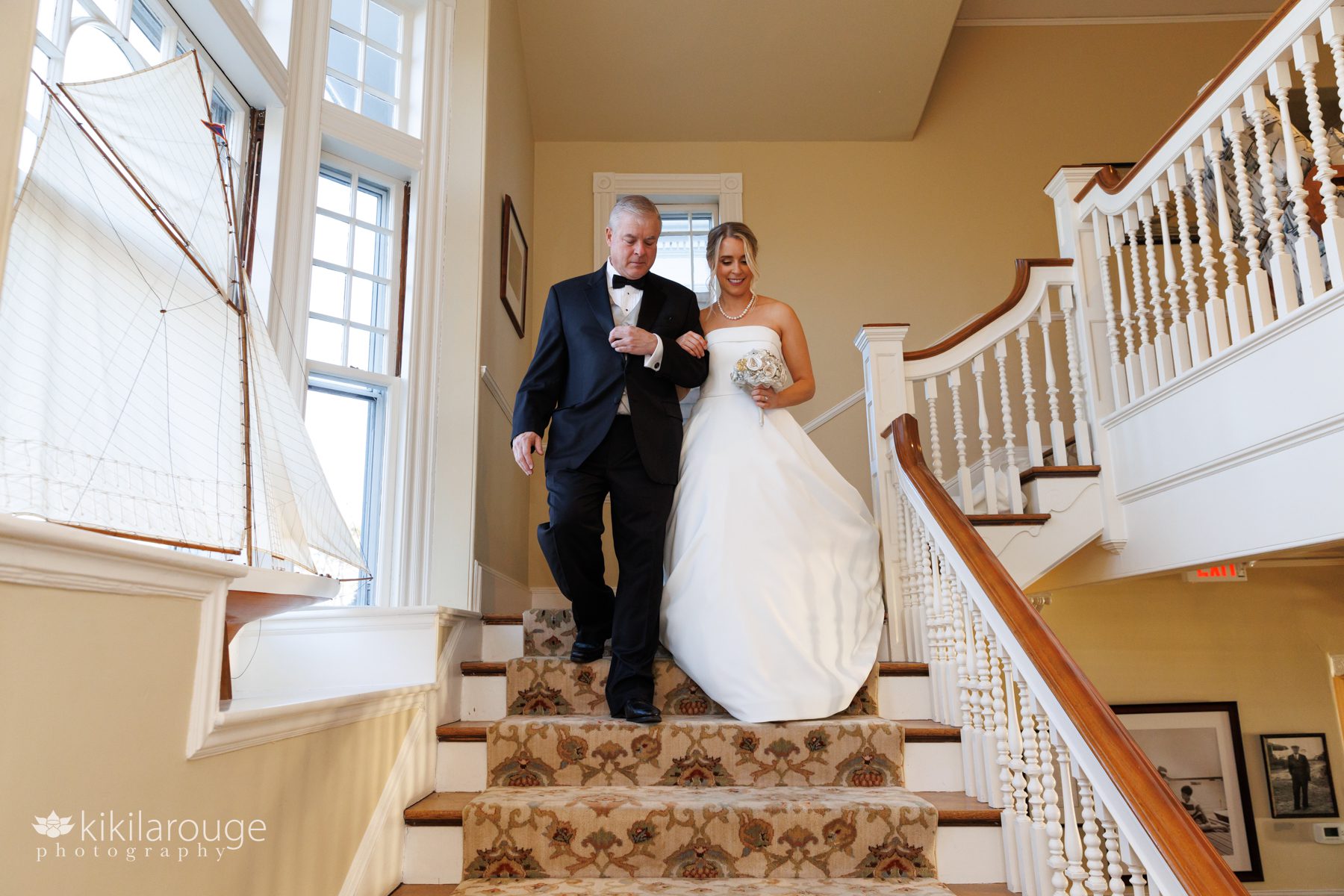 Father in tux walking bride down carpeted stairs at yacht club