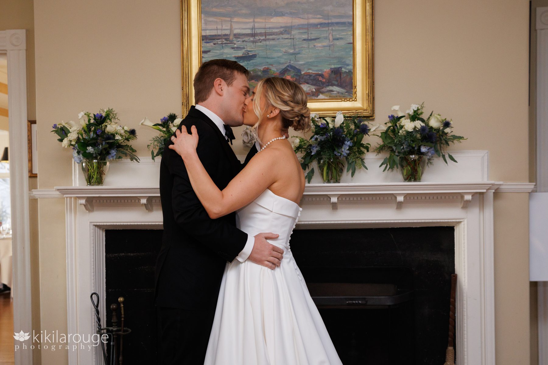 Wedding couples first kiss by fireplace with flowers on mantel