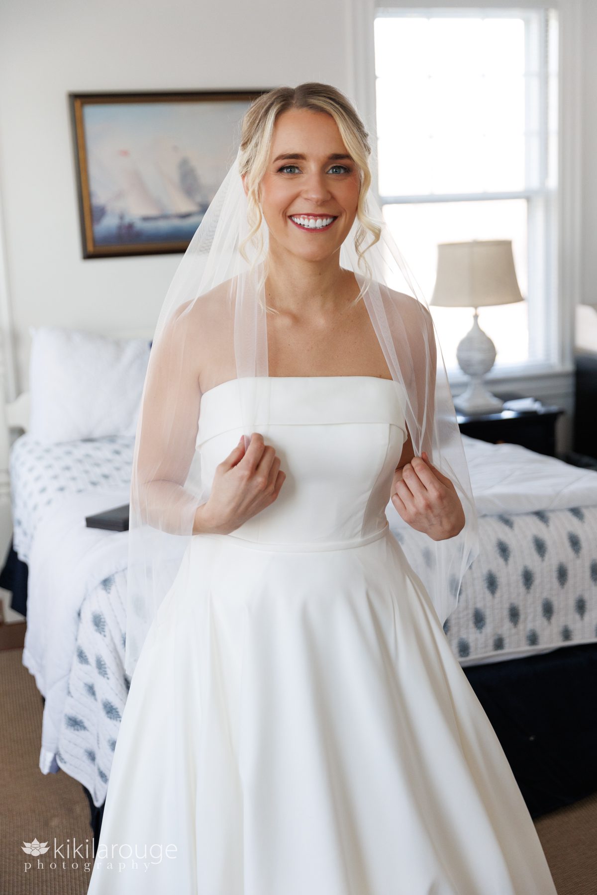 Bride in wedding dress holding veil with both hands smiling