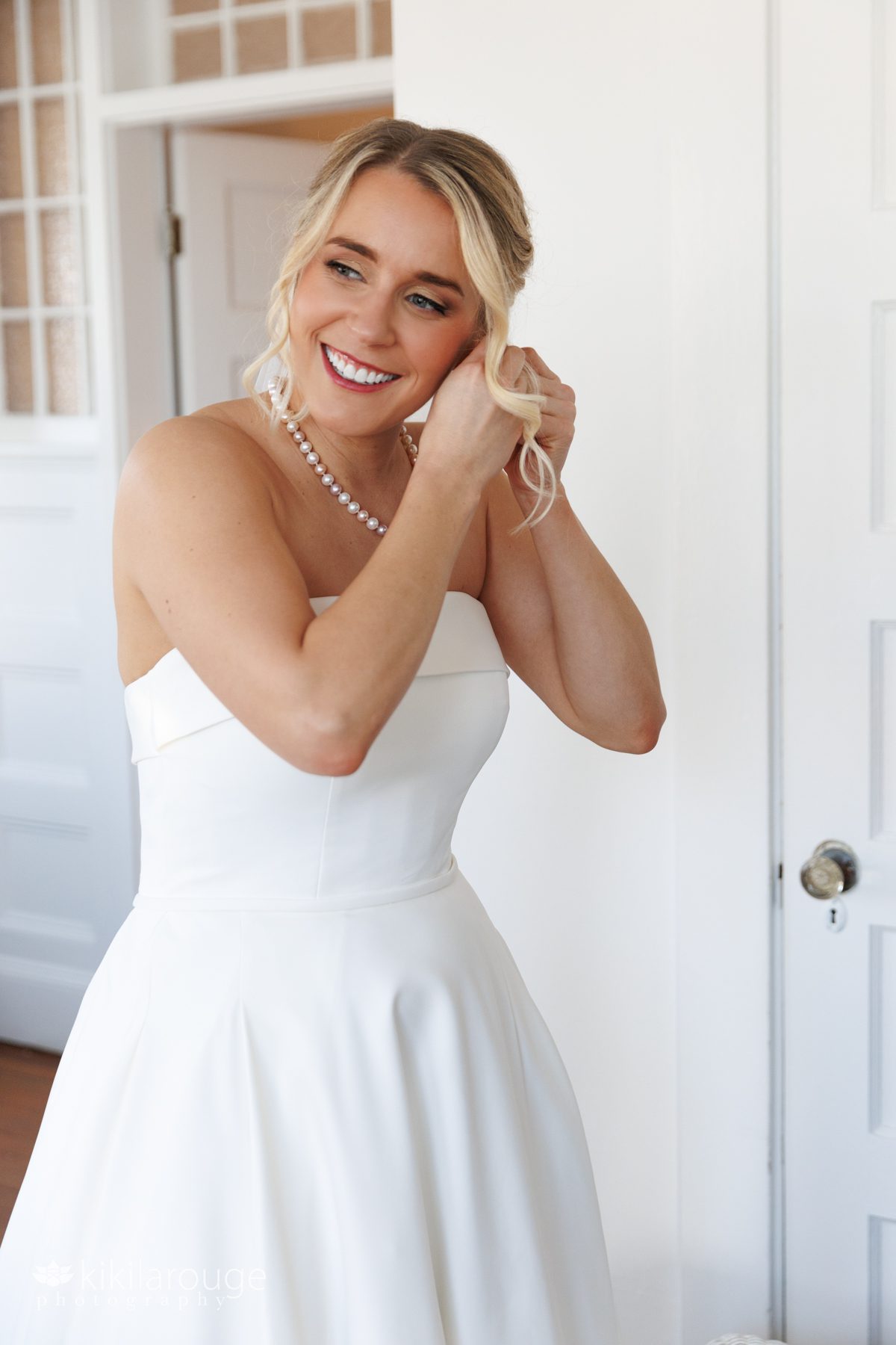 Bride with blonde hair and curls putting on earrings in bridal suite