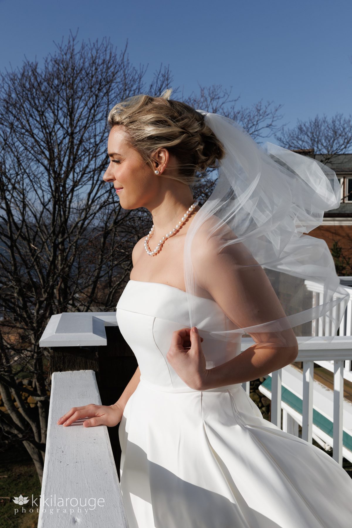 Profile of bride standing at the edge of a deck with the wind blowing hair and veil