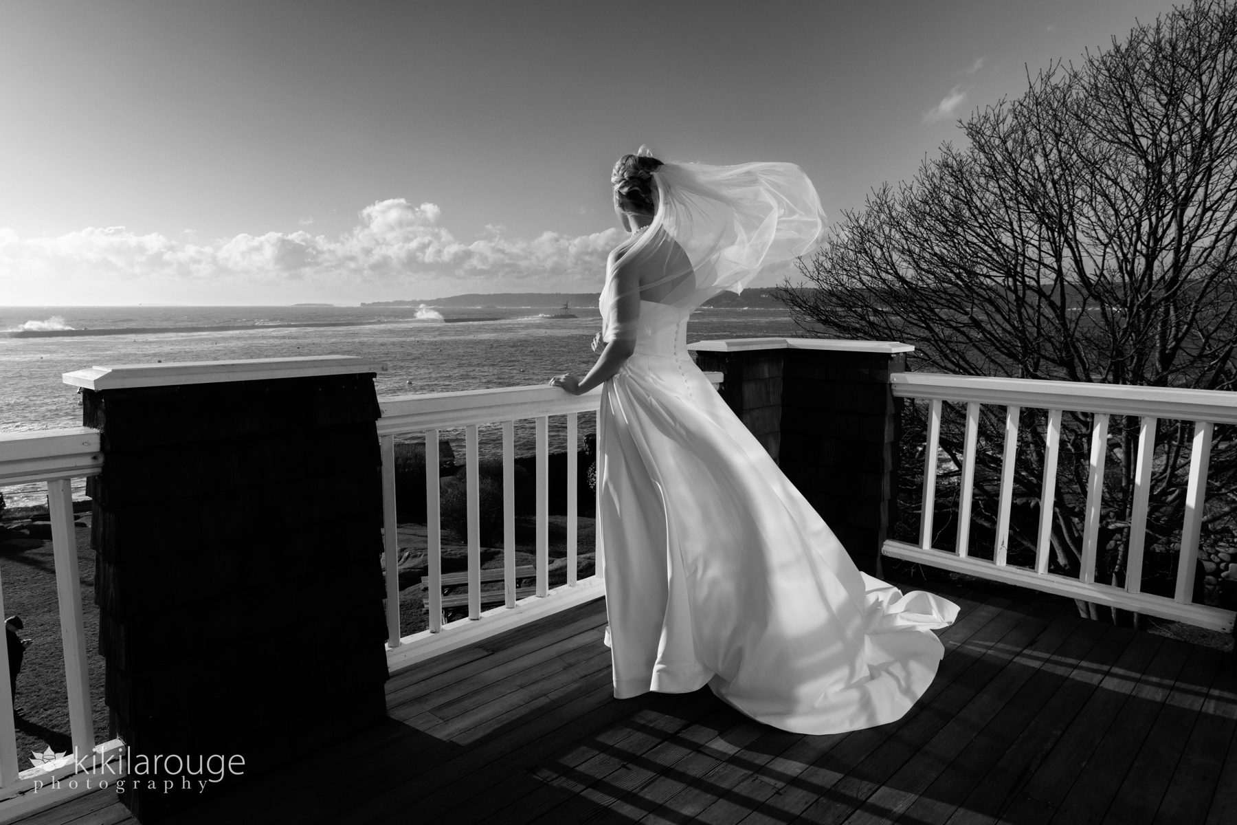 BW of bride standing at the edge of a deck with the wind blowing hair and veil