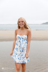 Teen girl in pretty blue and white sundress walking through a tidepool at Sandy Point beach laughing blonde hair blowing in wind