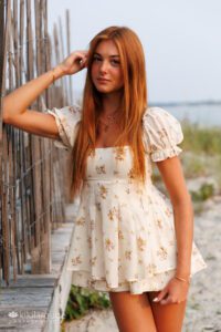 Teen girl looking serious leaning on weathered boardwalk at beach in flowered romper