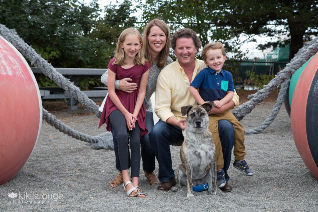 Family of four sitting on ropes attached to nautical structures in West Seattle with brindle rescue dog