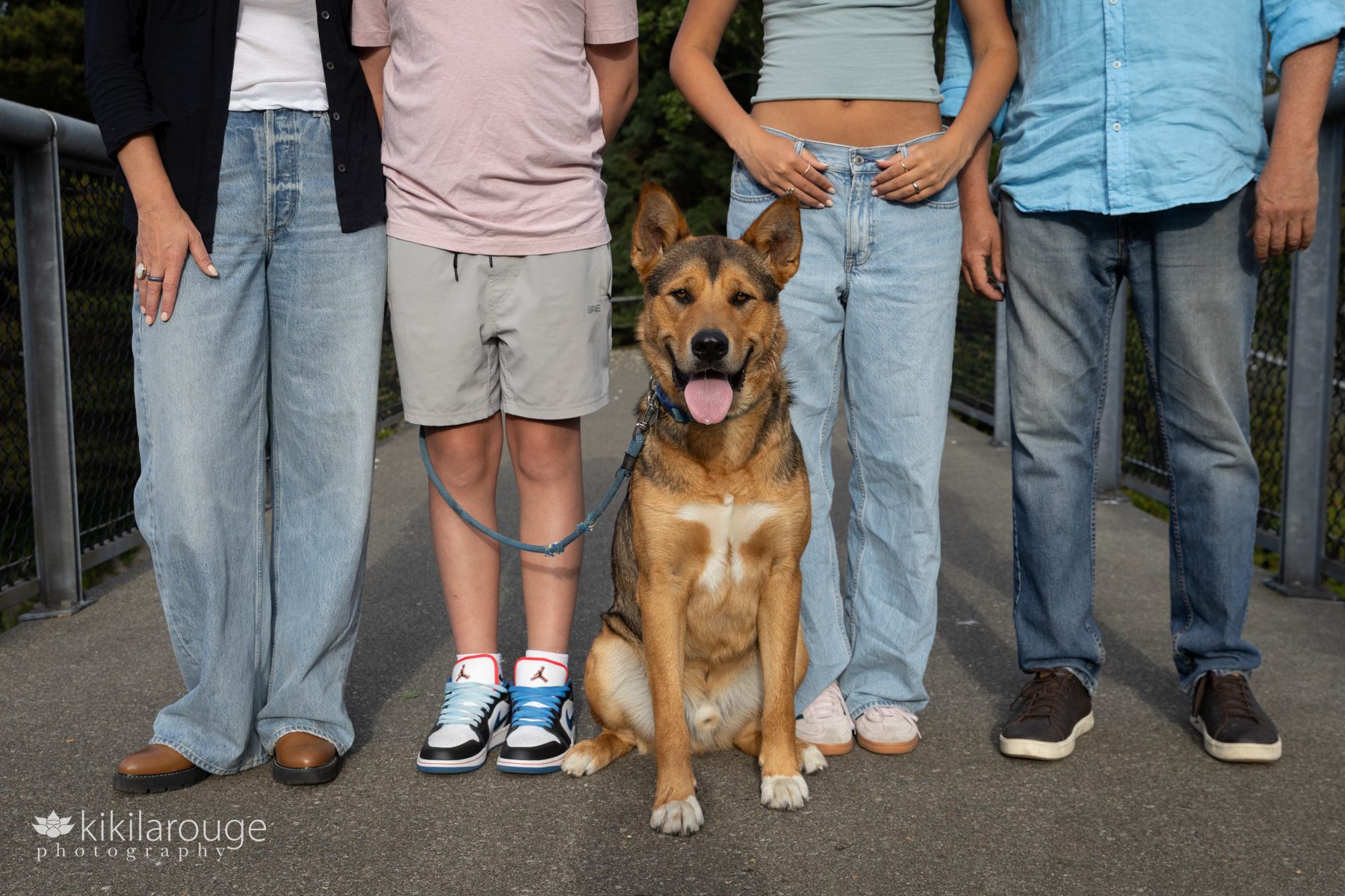 Lower half of family of four with their rescue dog sitting at their feet looking at the camera