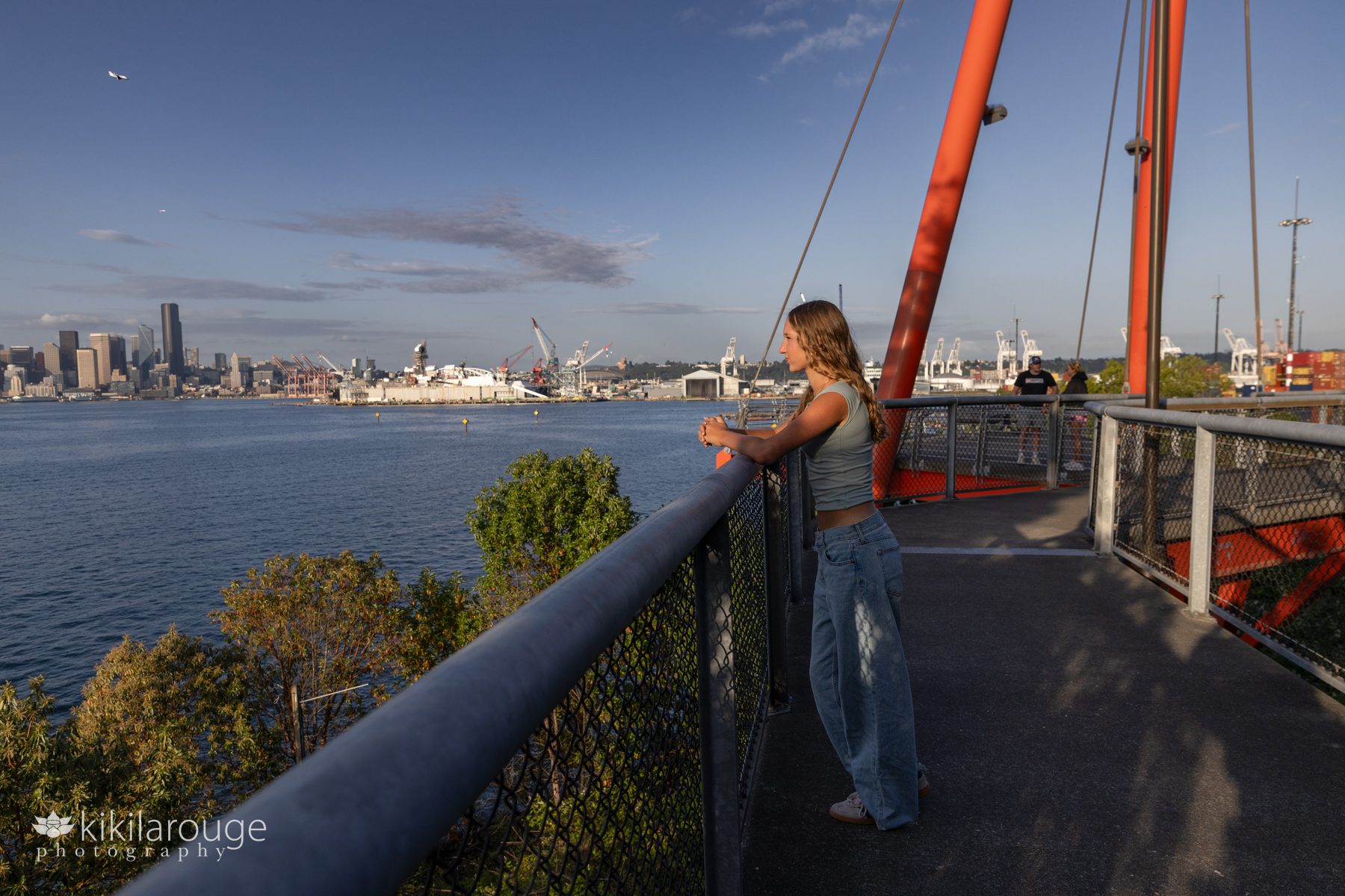 Teen girl in jeans in crop top looking out in profile on the Seattle skyline with two planes flying overhead