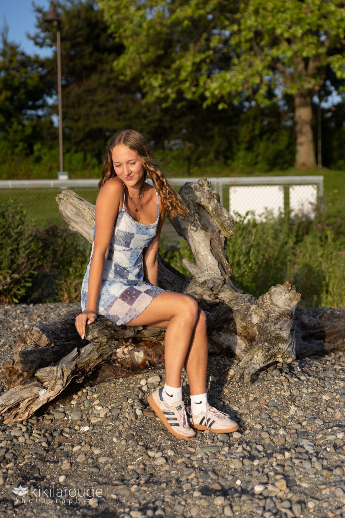 Teen girl with long blonder curly hair sitting on driftwood at rocky Seattle beach