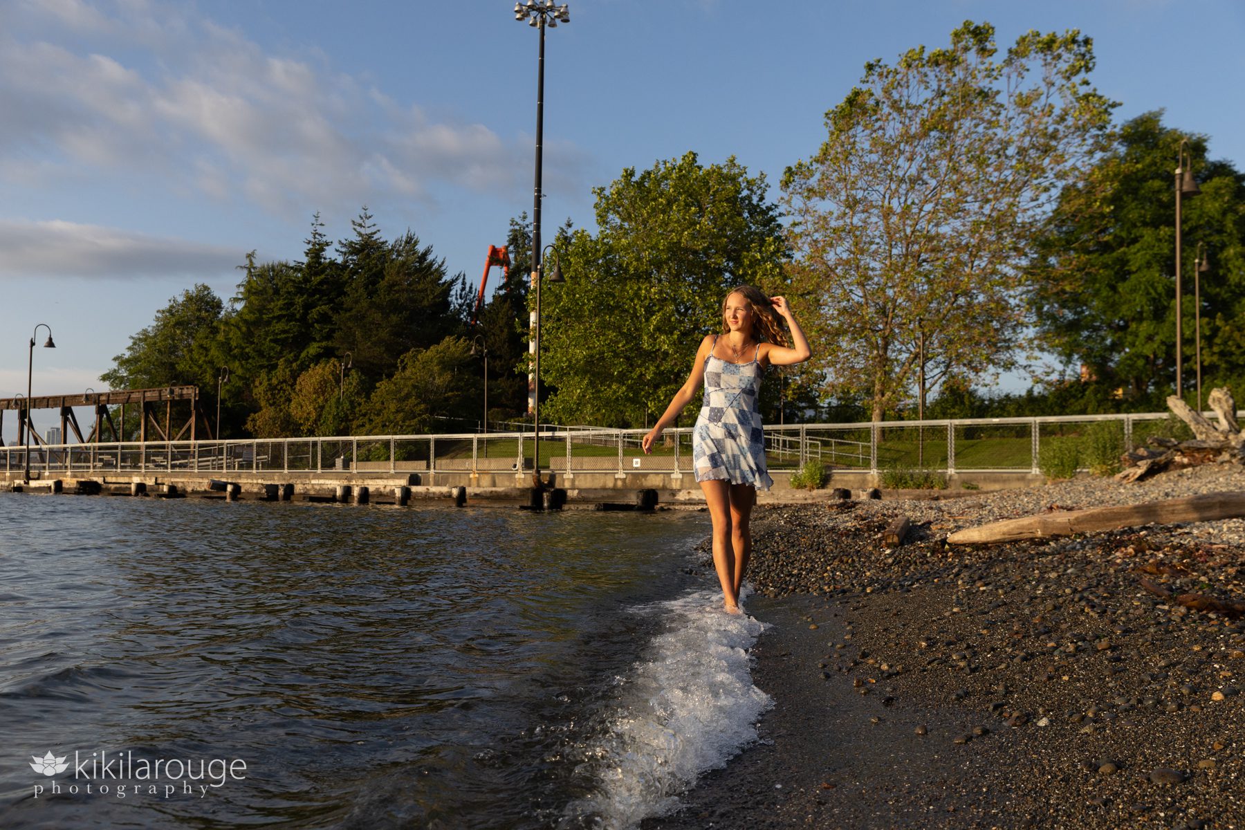 Teen girl walking along rocky Seattle beach at sunset with hands in hair