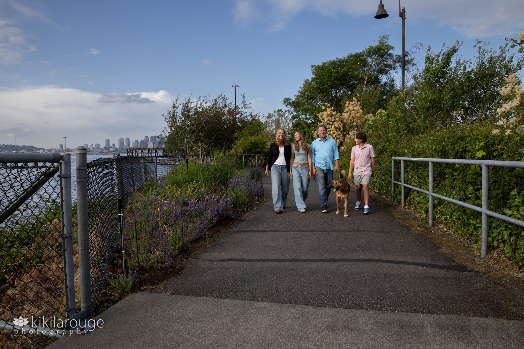 West Seattle family walking family dog along path at Jack Block Park with the Seattle Space Needle and skyline in the backdrop.