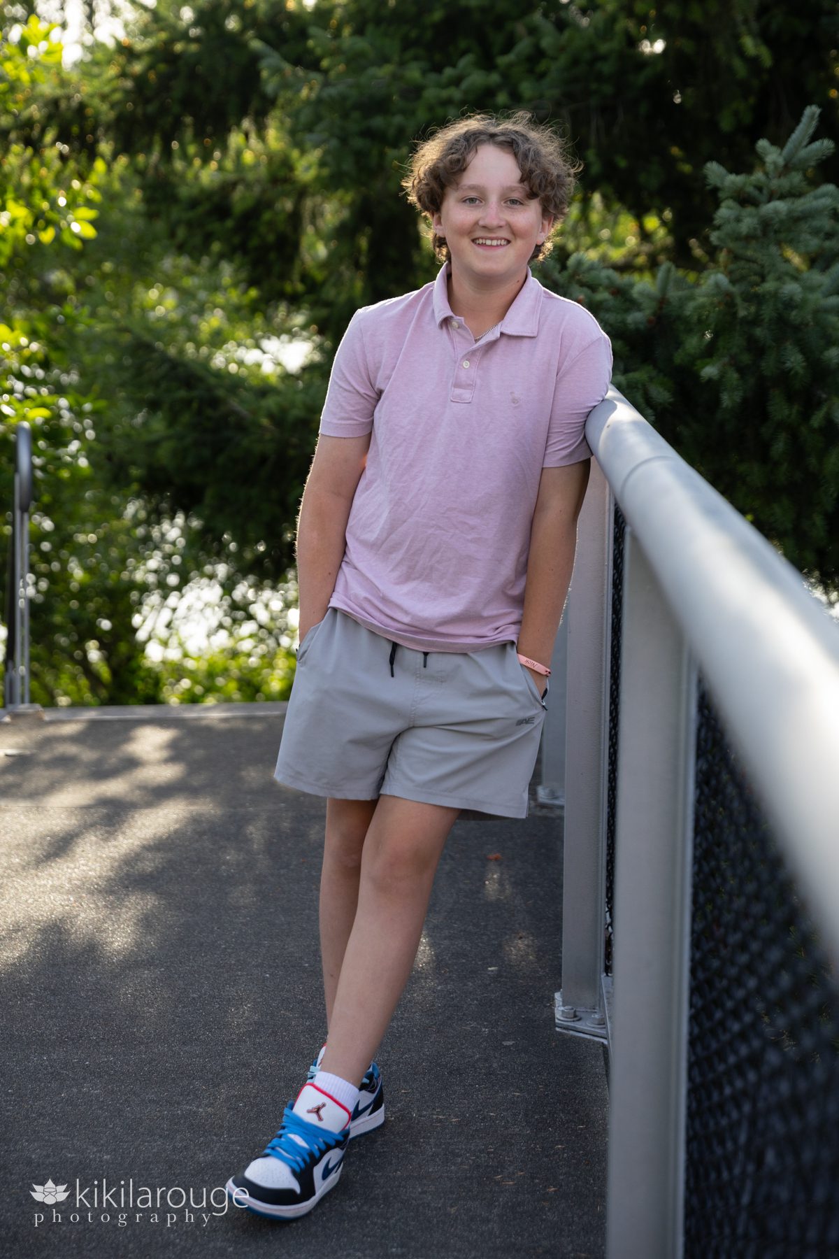Teen boy smiling in pink polo shirt leaning on bridge metal rail
