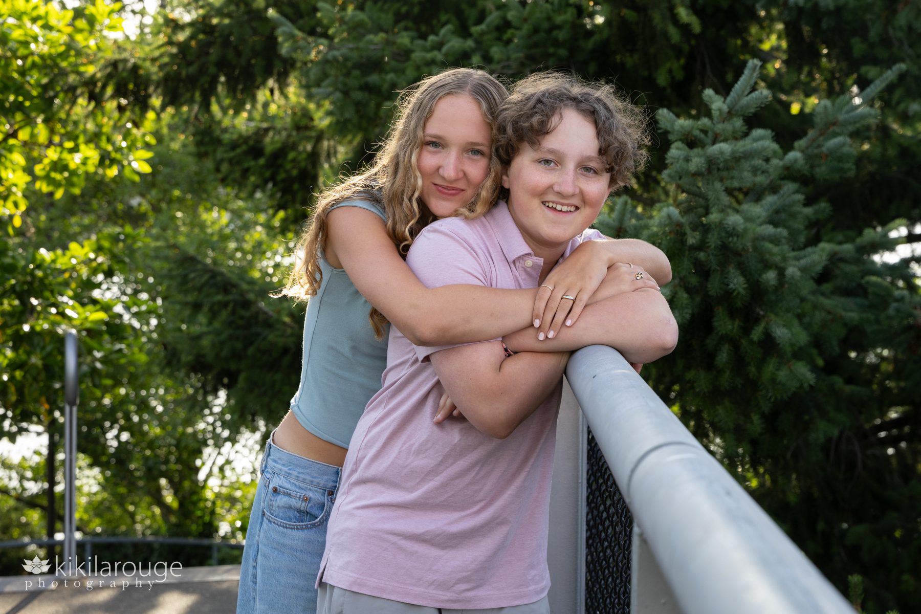 Teen brother and sister hugging and leaning on metal railing on West Seattle bridge