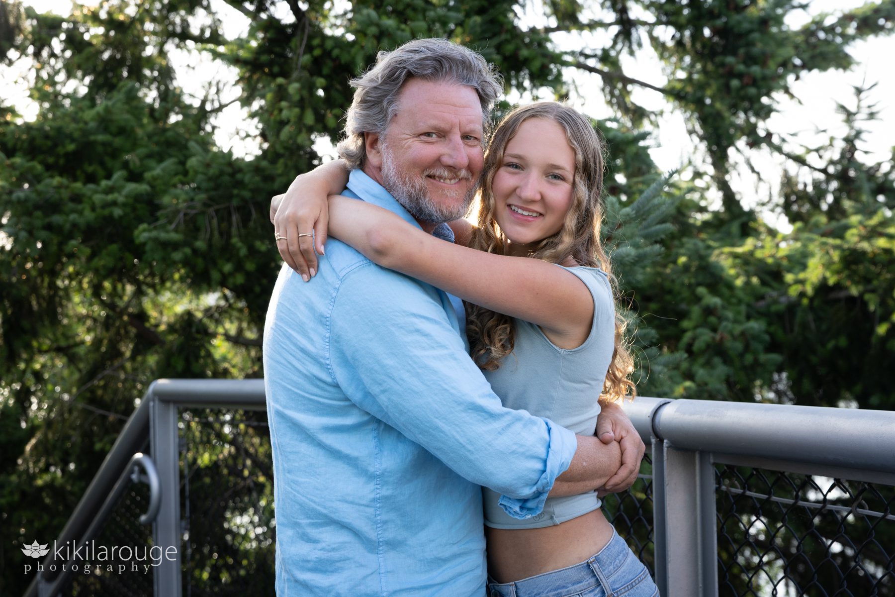 Dad in blue shirt hugging his teen daughter on metal bridge