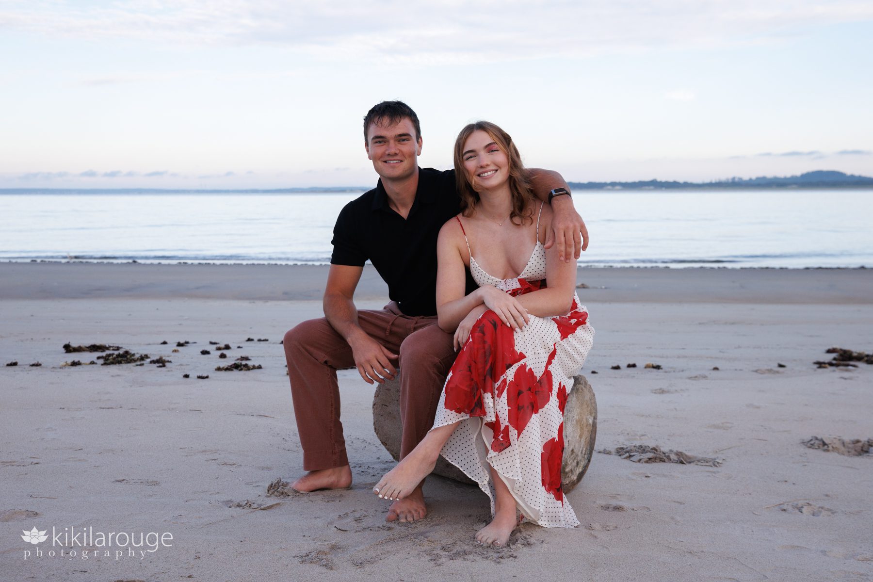 Brother and sister sitting on driftwood log at beach with Ipswich in backdrop
