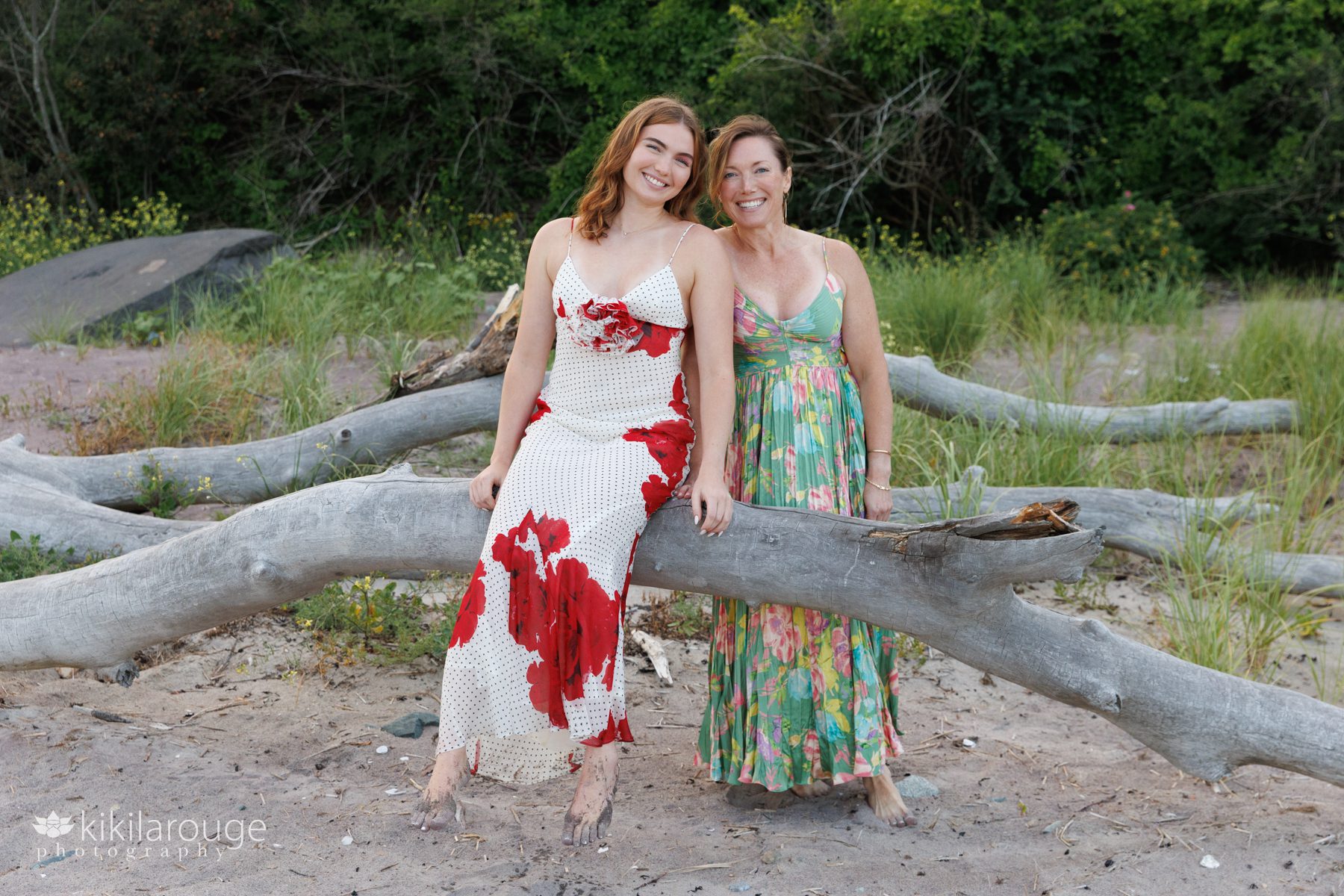 Mom and daughter in long summer dresses sitting on large driftwood at Sandy point beach