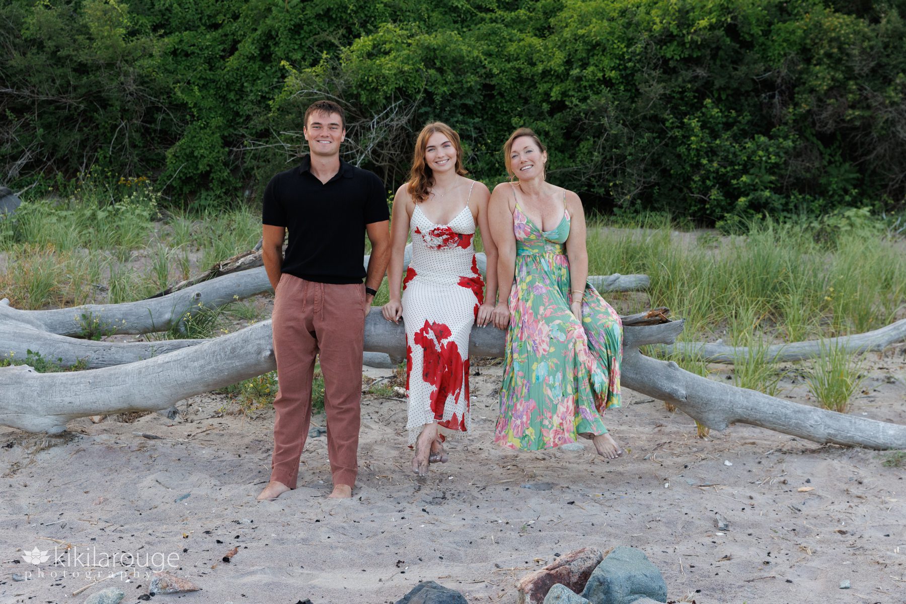 Family of three in long summer dresses sitting on large driftwood at Sandy point beach