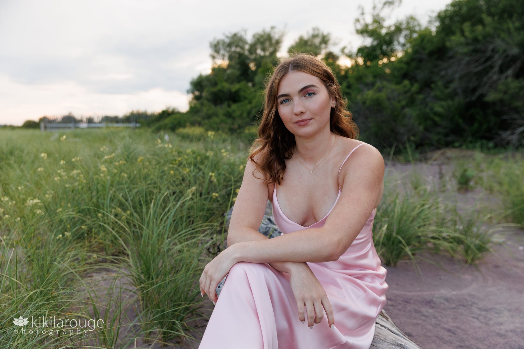 Girl in satin pink dress sitting on driftwood with yellow flowers in backdrop at Sandy Point