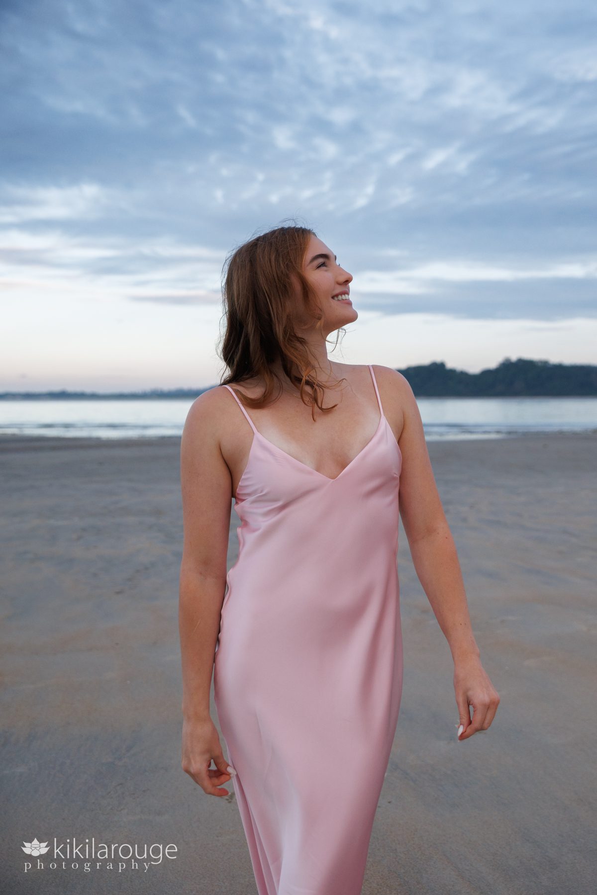 Teen girl smiling looking up at beach standing with a long pink sating dress
