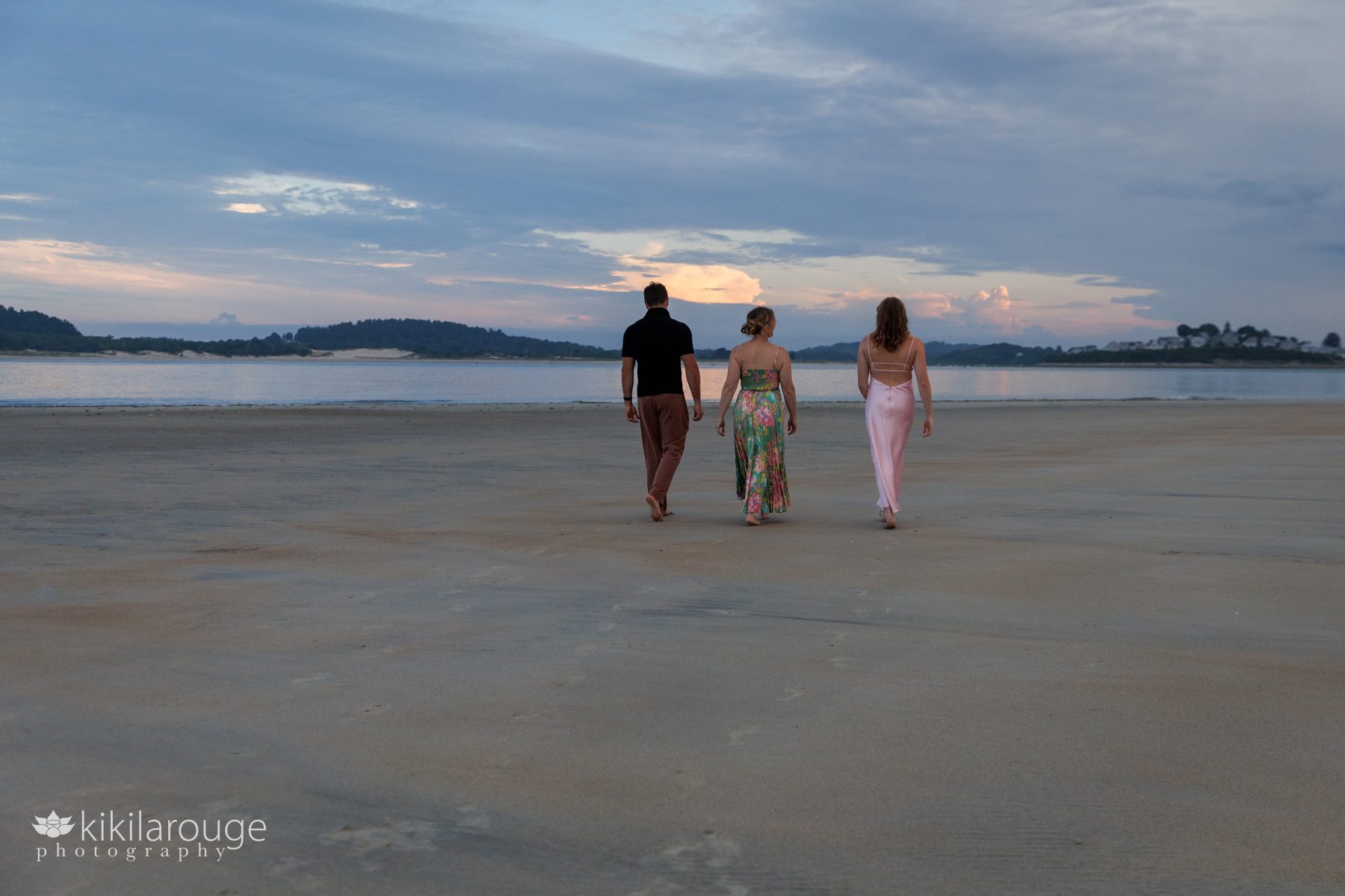 Family of three walking away at sunset with footprints in the sand into the dramatic Sandy Point sunset