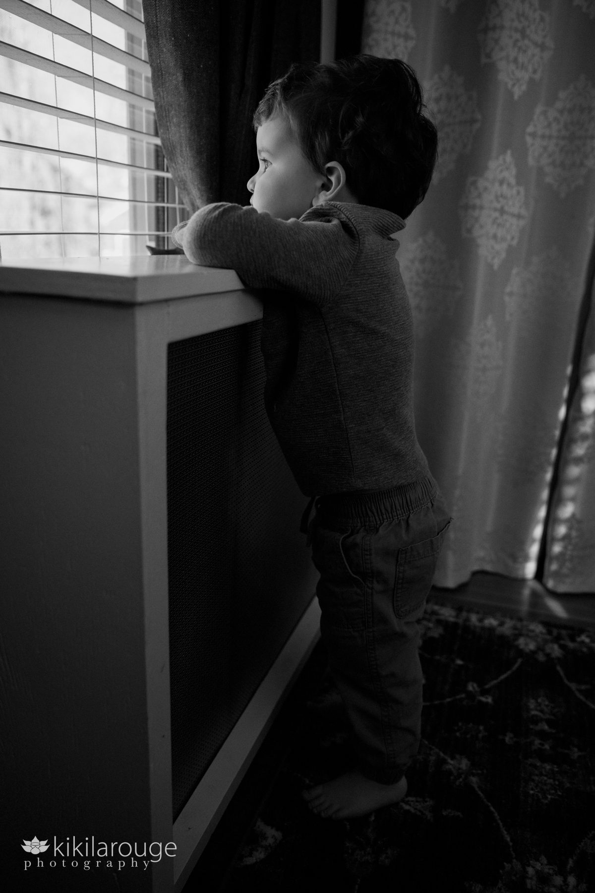 Three year old boy leaning and looking out window