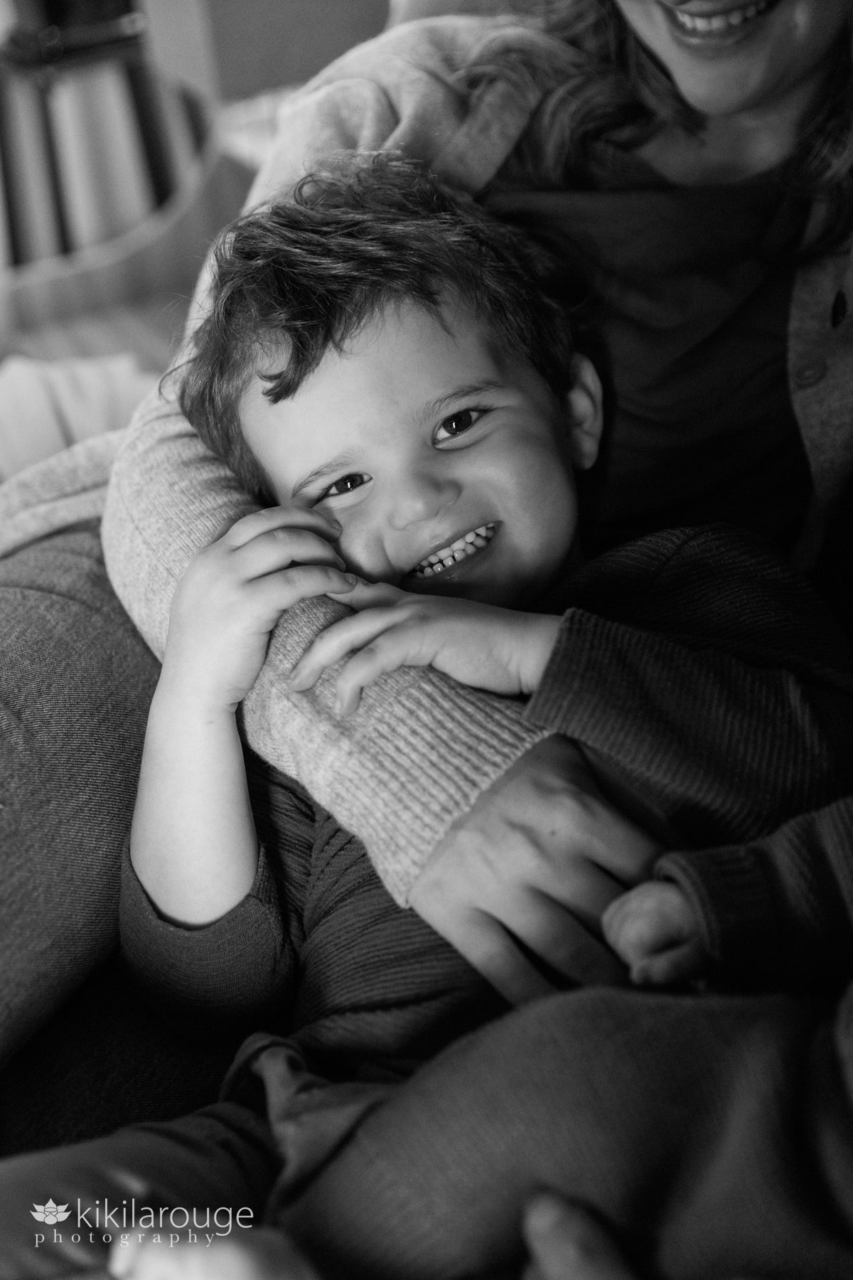 Three year old boy snuggling in bed smiling in Mom's arms