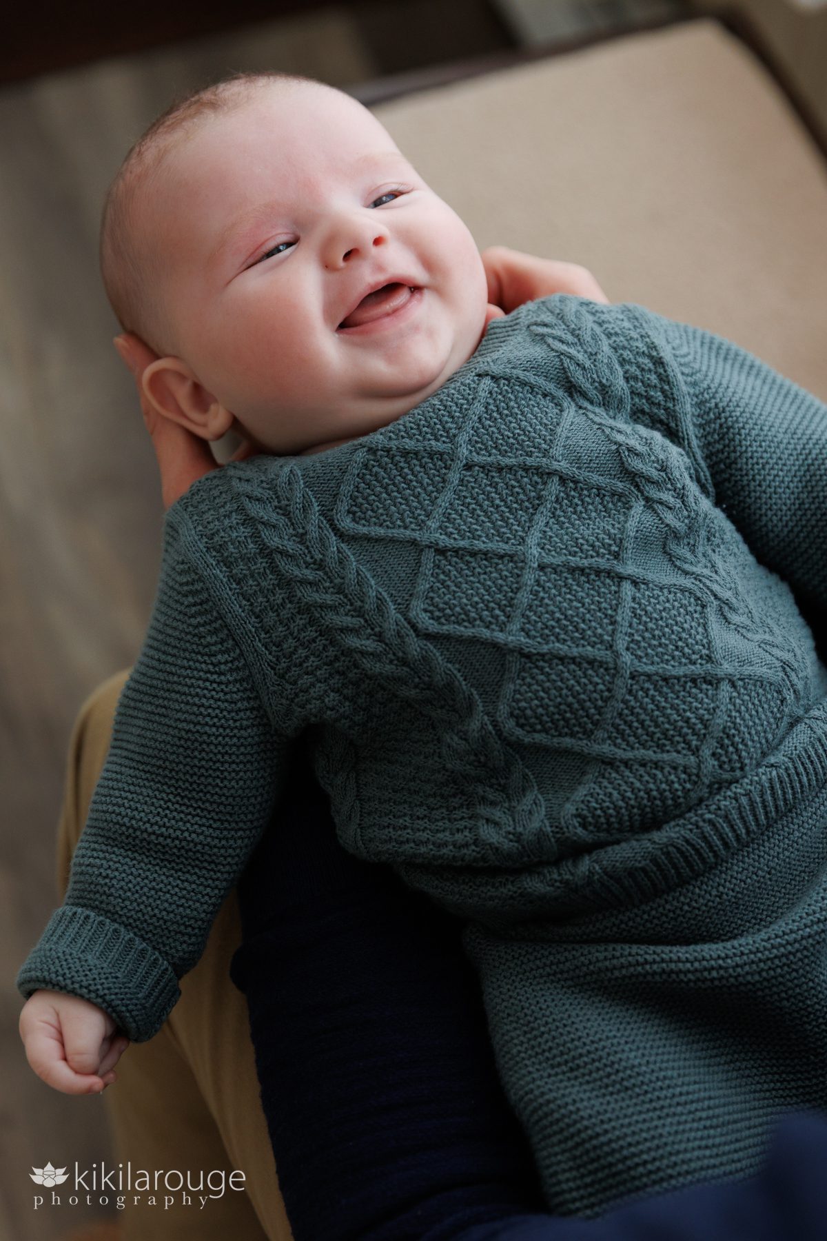 Smiling two month old baby looking up at her Dad in forest green cable sweater and pants