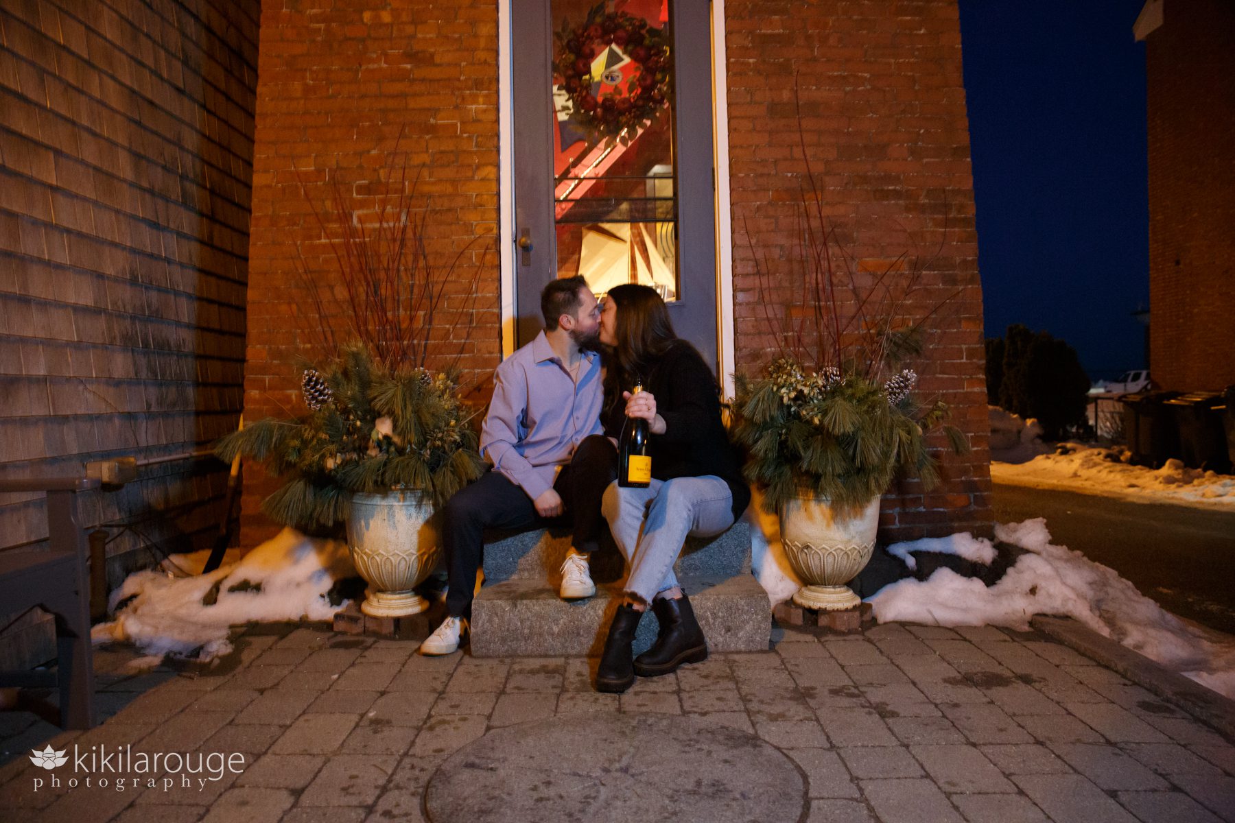 Couple sitting with champagne on lighthouse steps during the blue hour with snow on the ground