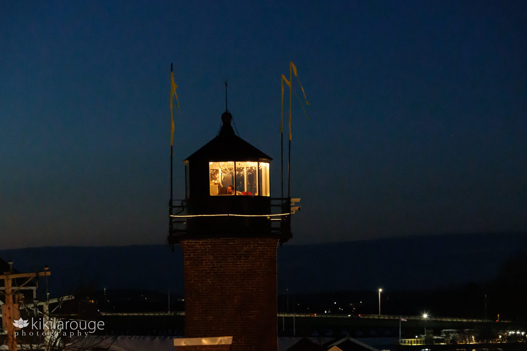 Ariel view of couple kissing in lighthouse at blue hour with yellow flags blowing