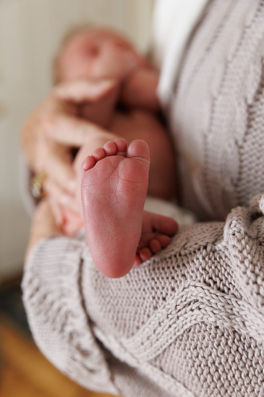 Close up of newborn baby's feet while being held by his Grandmom who is wearing beige sweater