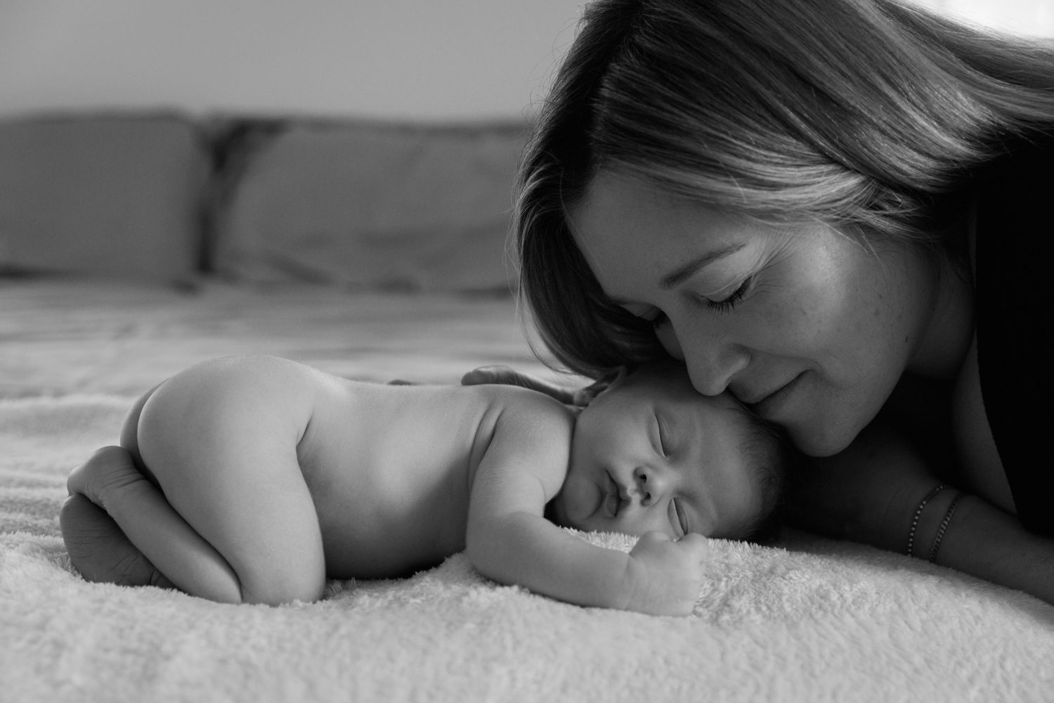 Naked newborn baby sleeping on bed with Mom snuggled next to him